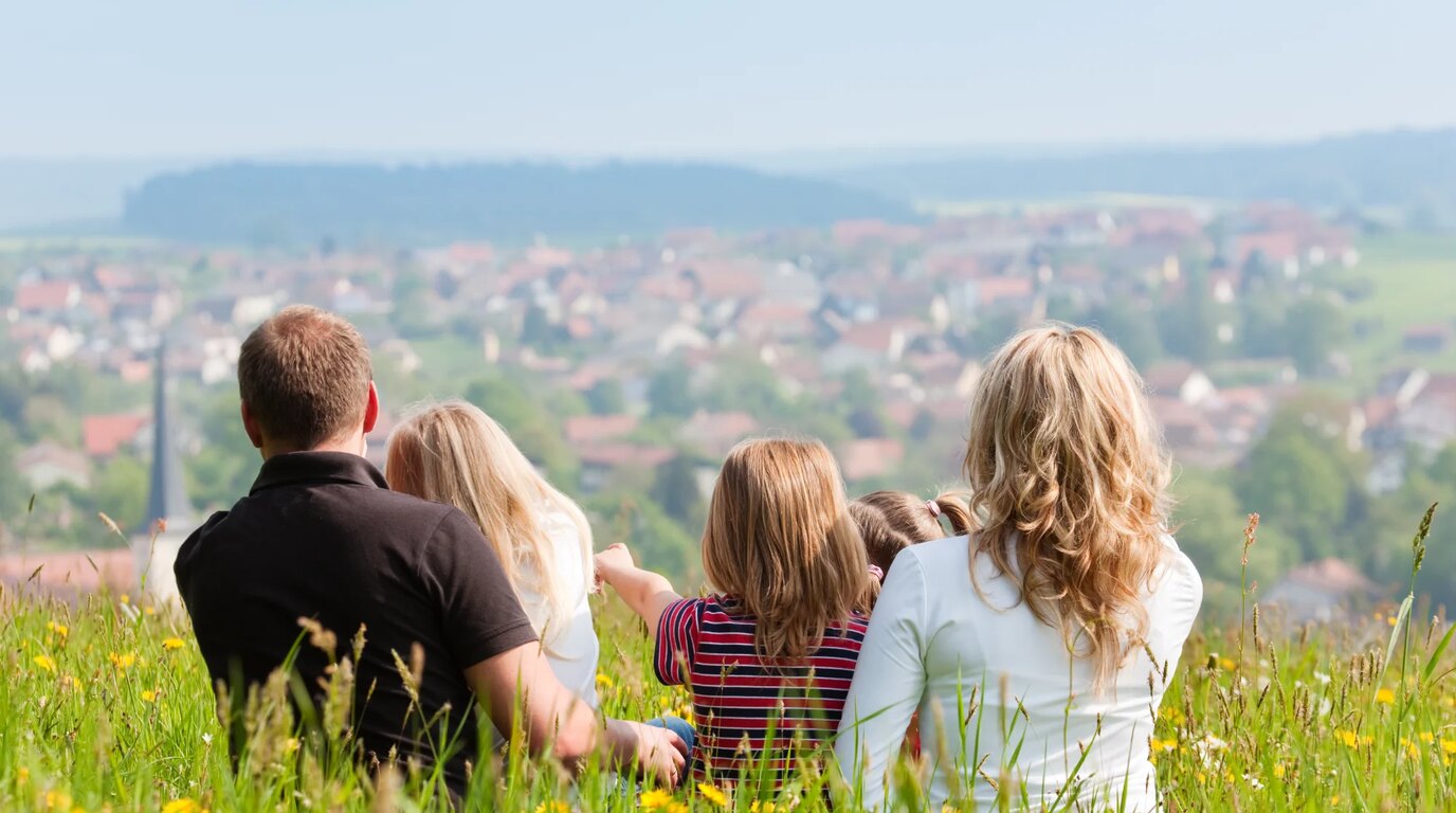 A family sitting on a grassy hillside looking out over a neighborhood below